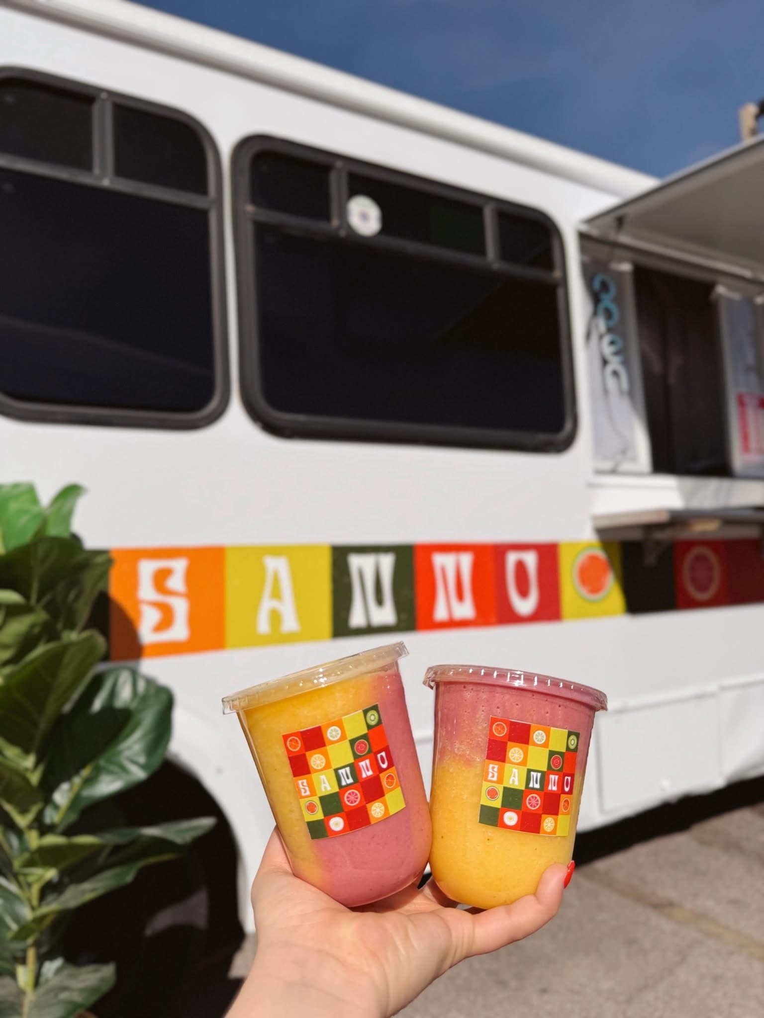 Two fresh SANNO smoothies held up in front of the SANNO food truck